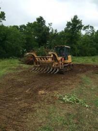 Yellow bulldozer clearing muddy ground in a wooded area