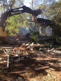 John Deere excavator clearing debris at a demolished site with trees in the background
