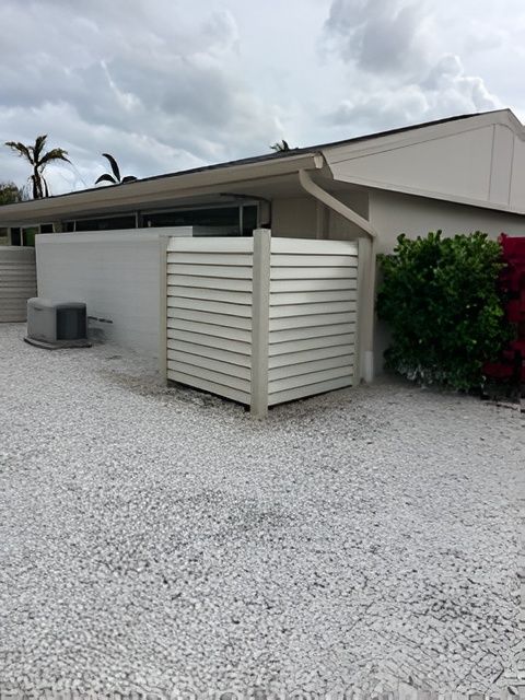 A beige home exterior with a louvered privacy screen shielding an air conditioning unit over a white gravel yard.