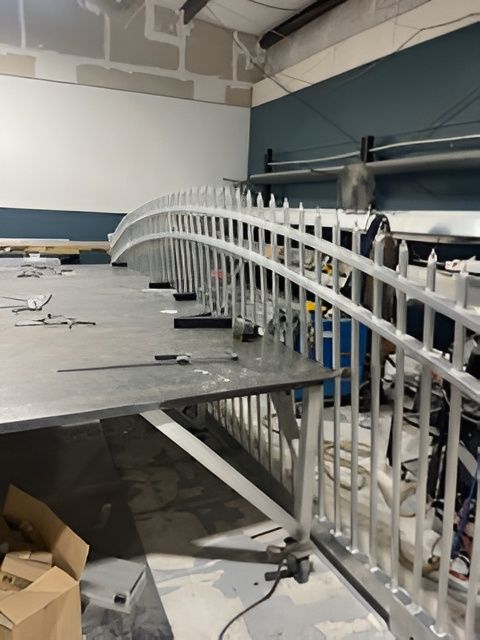 A curved metal fence section rests on a workshop table, with a metal ruler and tools nearby.