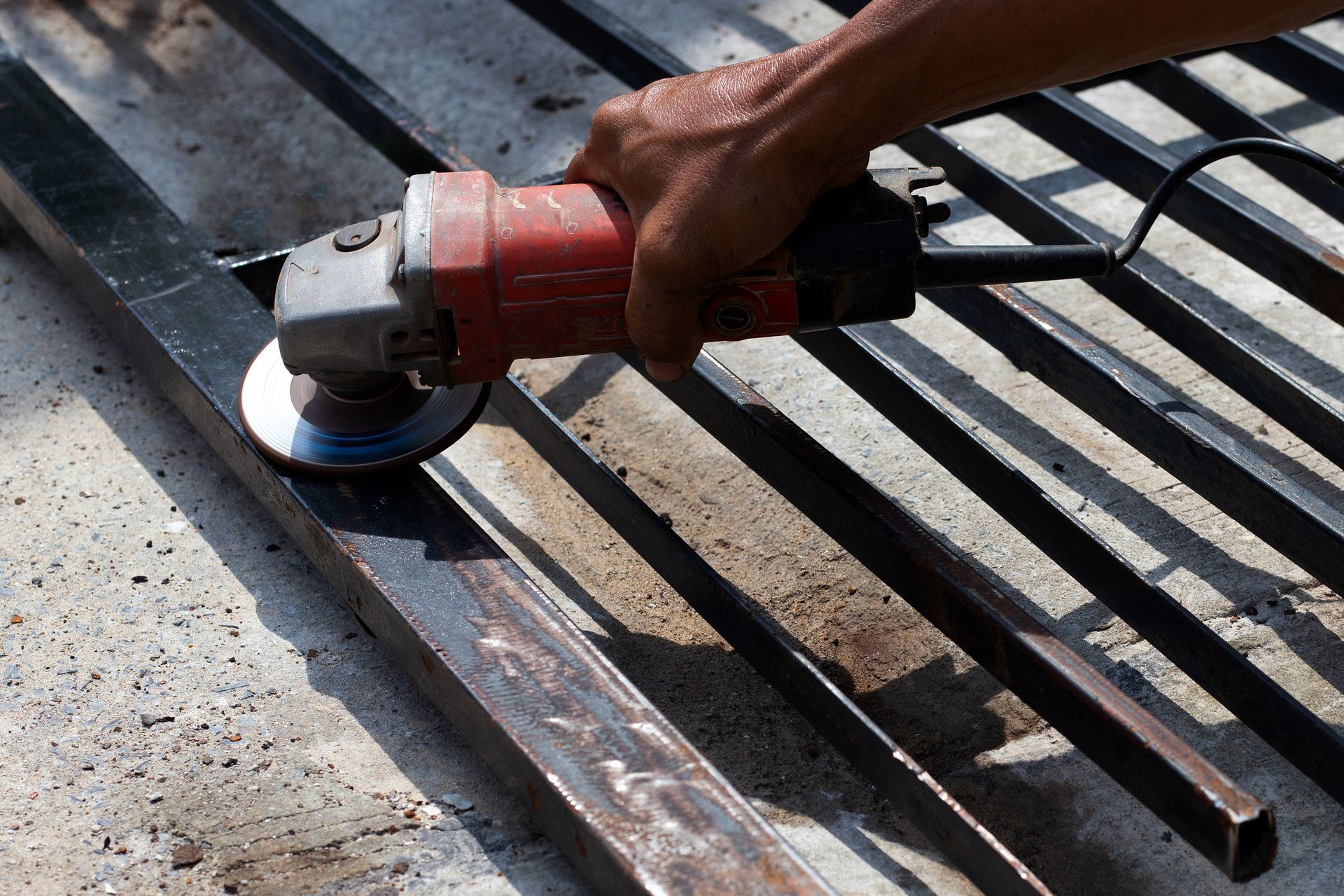 A hand uses an angle grinder to smooth a metal fence or gate outdoors.