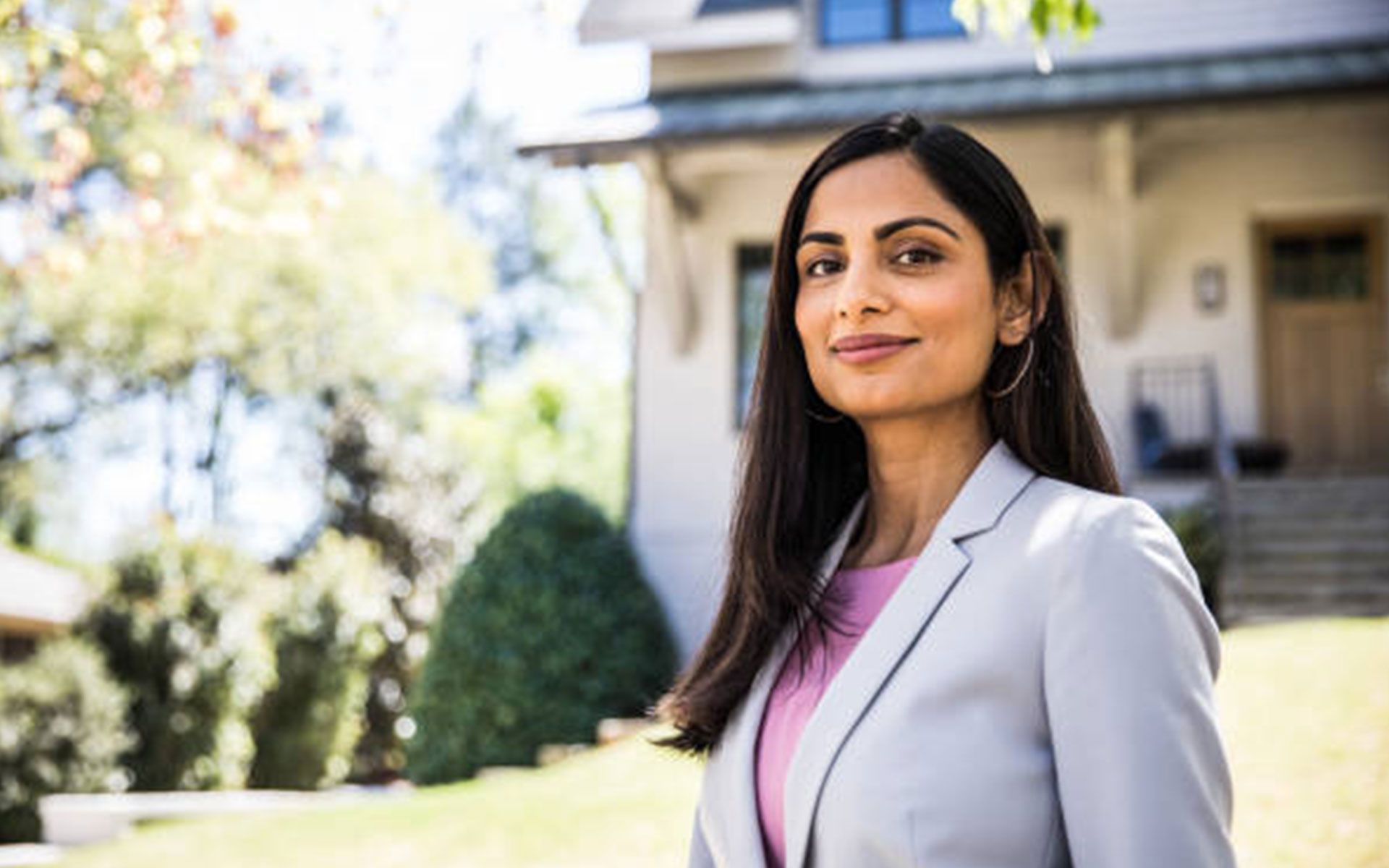 A woman in a suit is standing in front of a house.