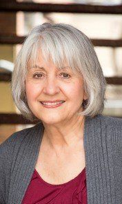 A woman with gray hair and a red shirt is smiling for the camera.