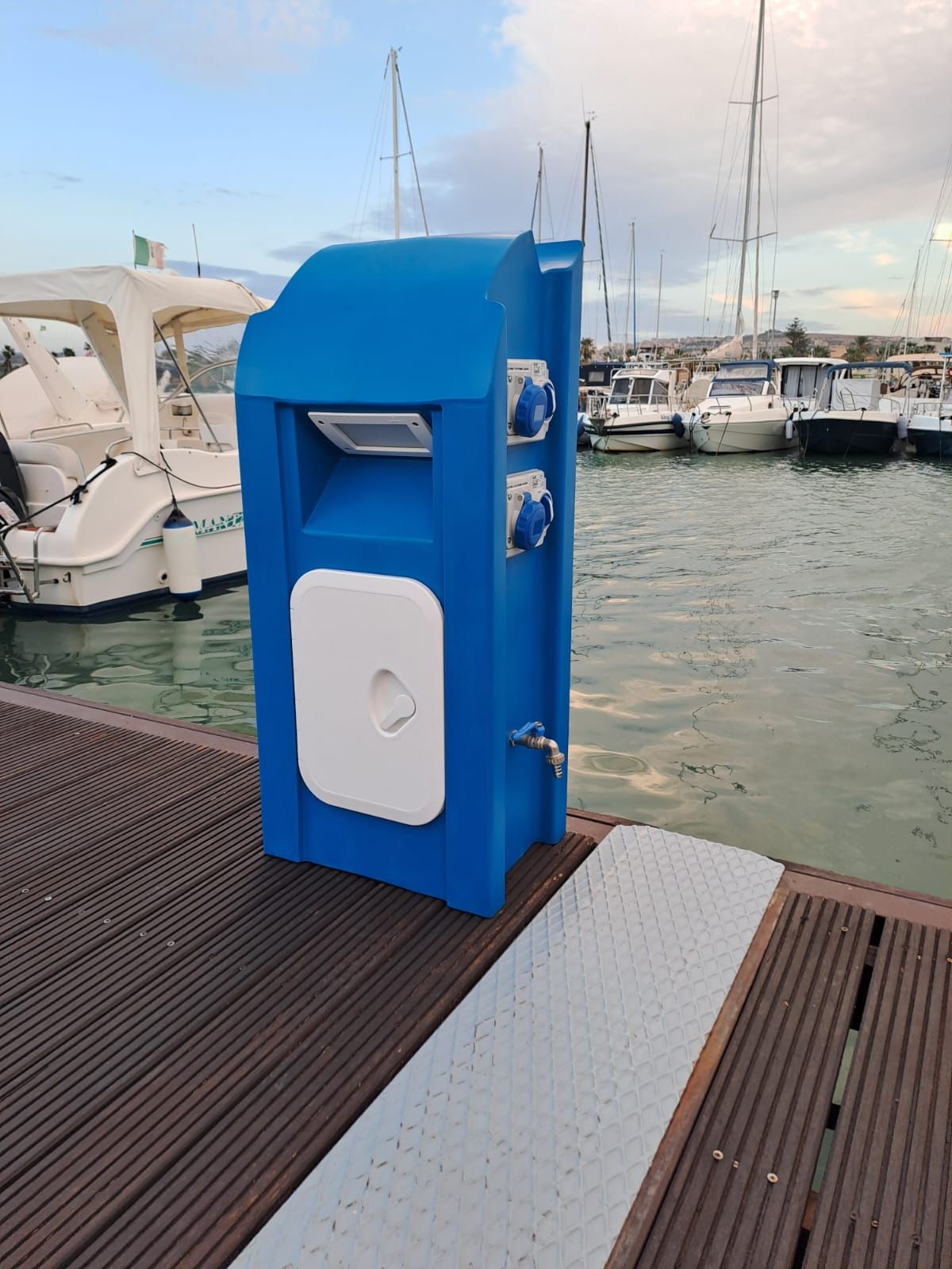 Cassetta di servizio blu da molo con prese elettriche e rubinetto dell'acqua, vicino alle barche.
