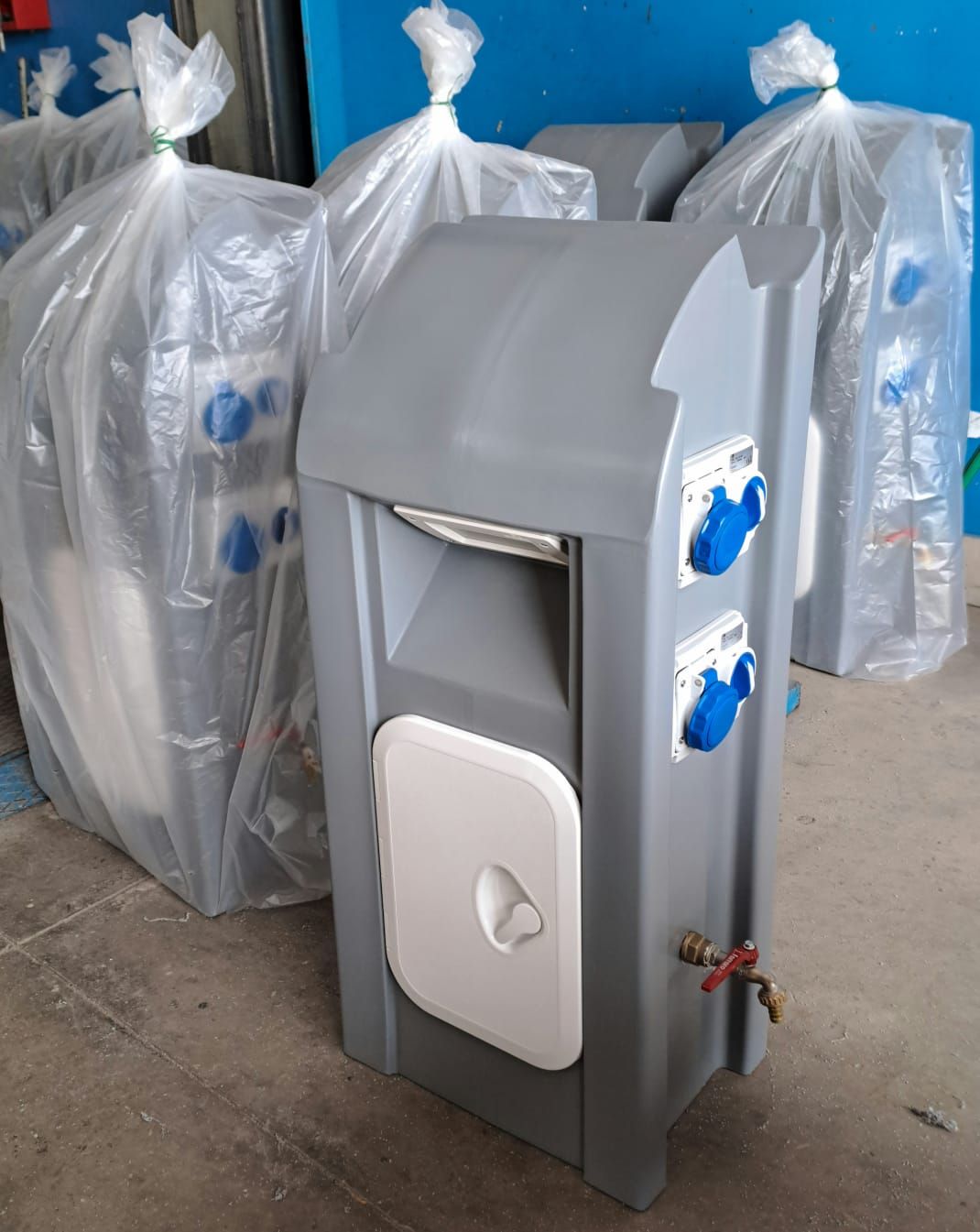 Unità di alimentazione portatili grigie, alcune avvolte nella plastica, con prese blu e una porta bianca.