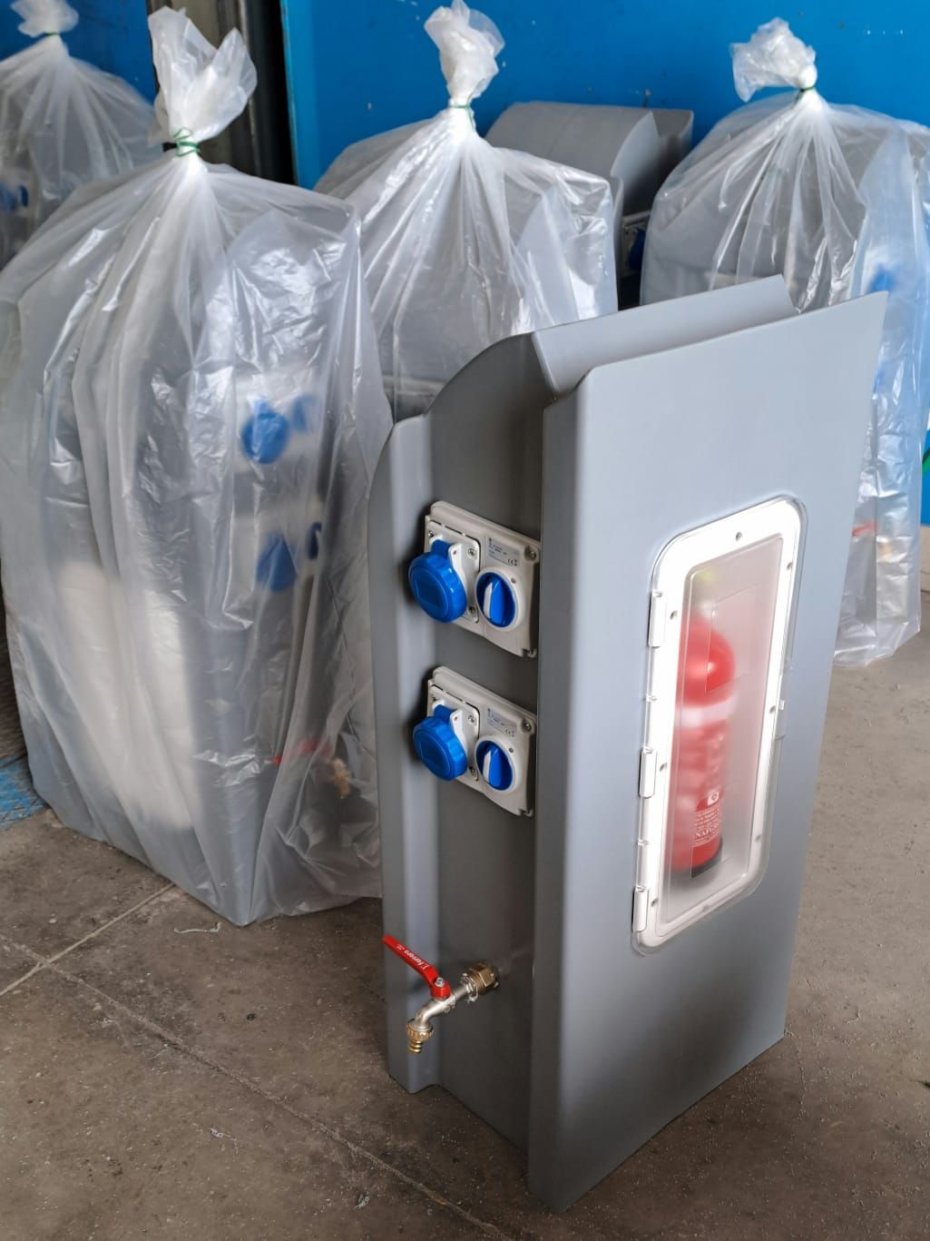 Mobile grigio con manopole blu, estintore rosso e rubinetto dell'acqua. Attrezzatura imballata sullo sfondo.