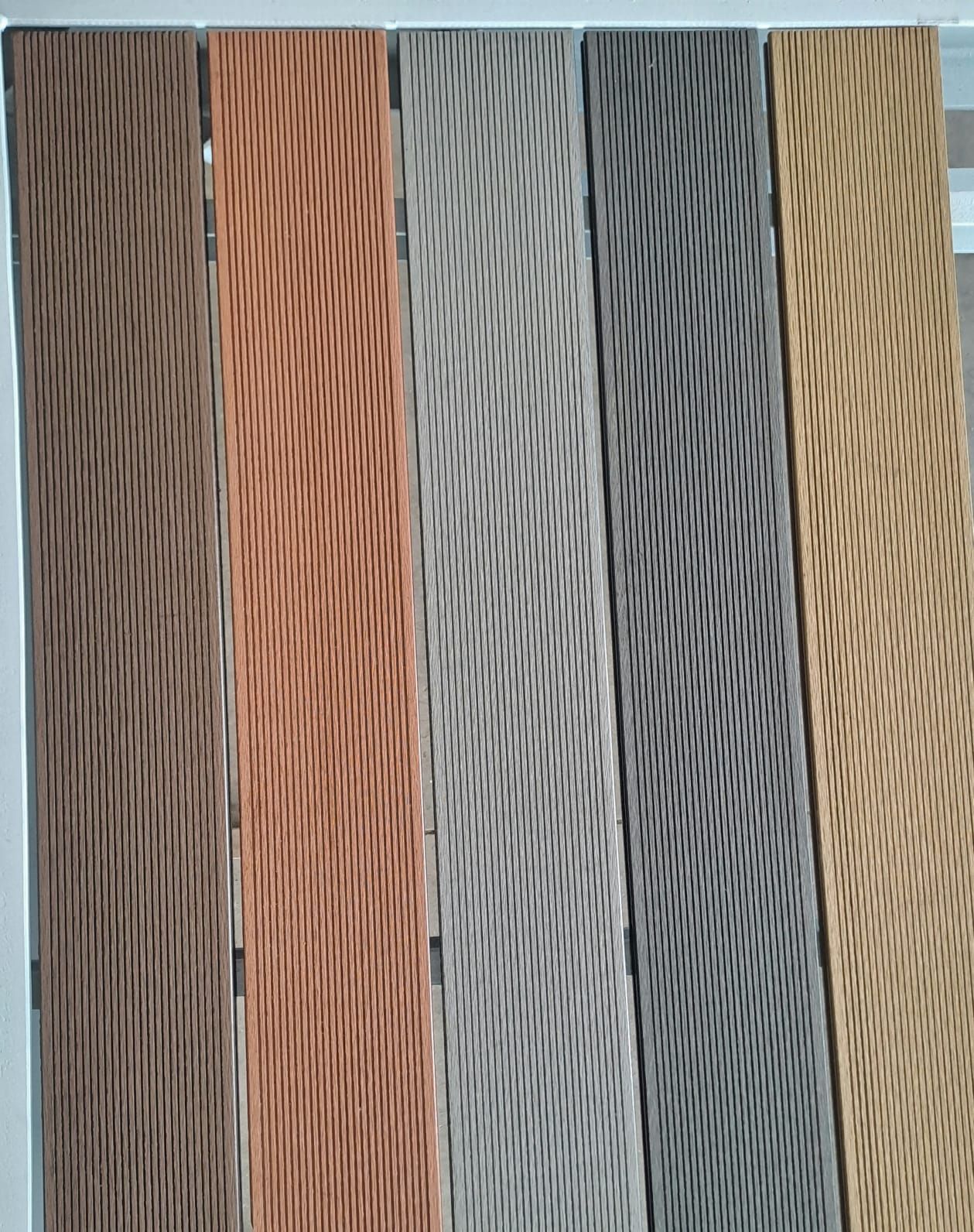 Cinque assi di pavimentazione composita in diverse tonalità di marrone, beige e grigio, con un motivo diagonale strutturato.