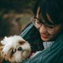 A woman wearing glasses is holding a small dog