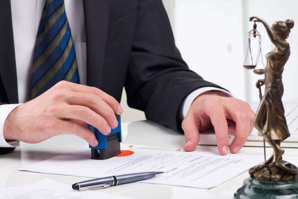 Un hombre está poniendo un sello en un trozo de papel al lado de una estatua de la justicia.