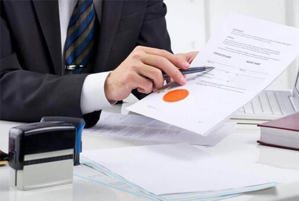 Un hombre con traje y corbata está sentado en un escritorio firmando un documento.