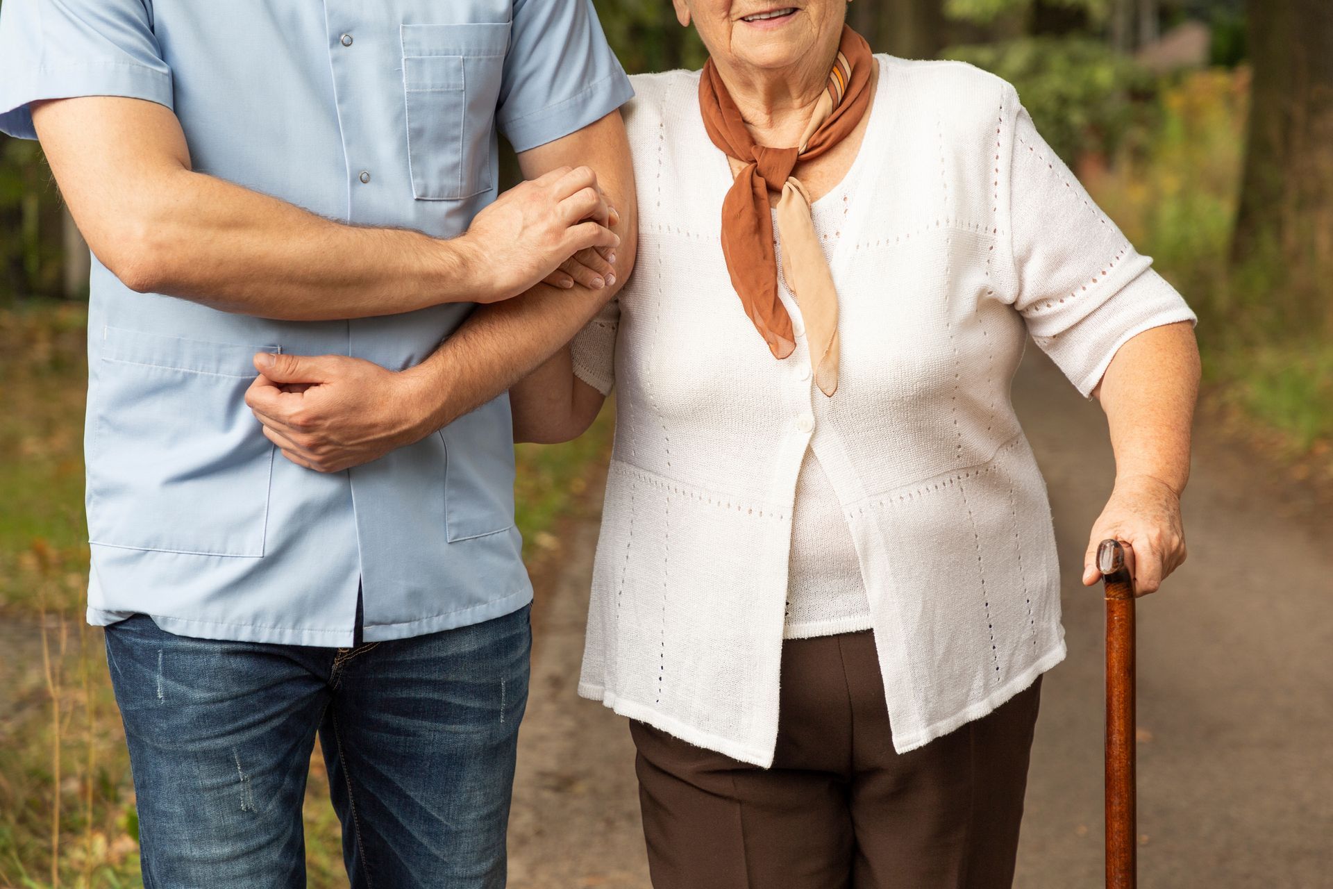 Un uomo aiuta un'anziana donna con un bastone a camminare lungo un sentiero.