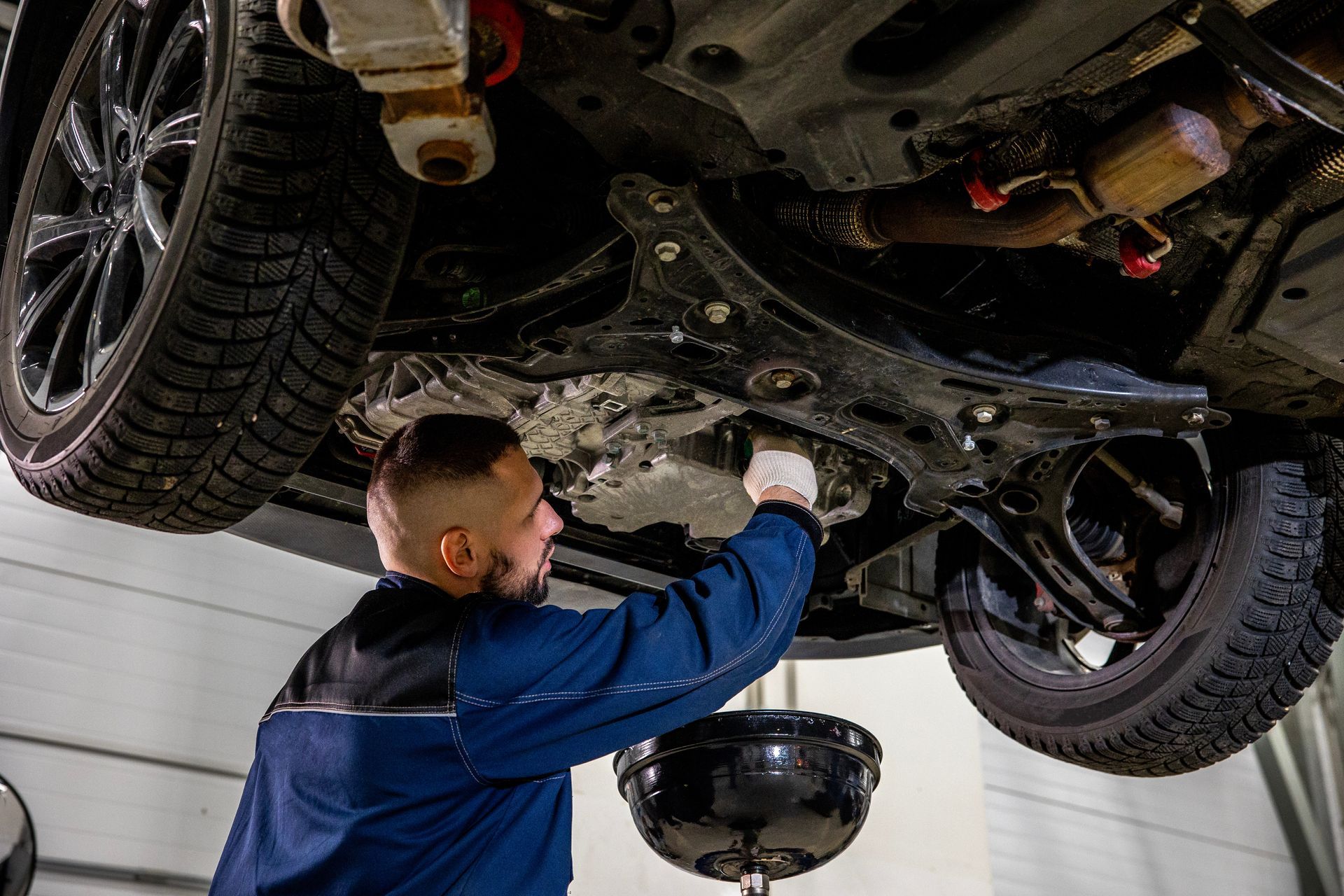 A mechanic performing an oil change under a raised car with a drain pan. A mechanic performing an oil change under a raised car with a drain pan.