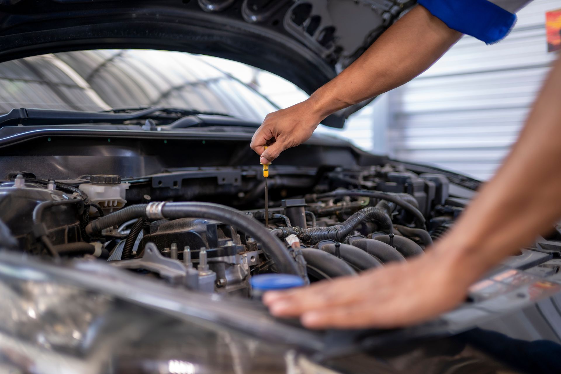 Mechanic checking engine oil with dipstick while holding an oil container under car hood.