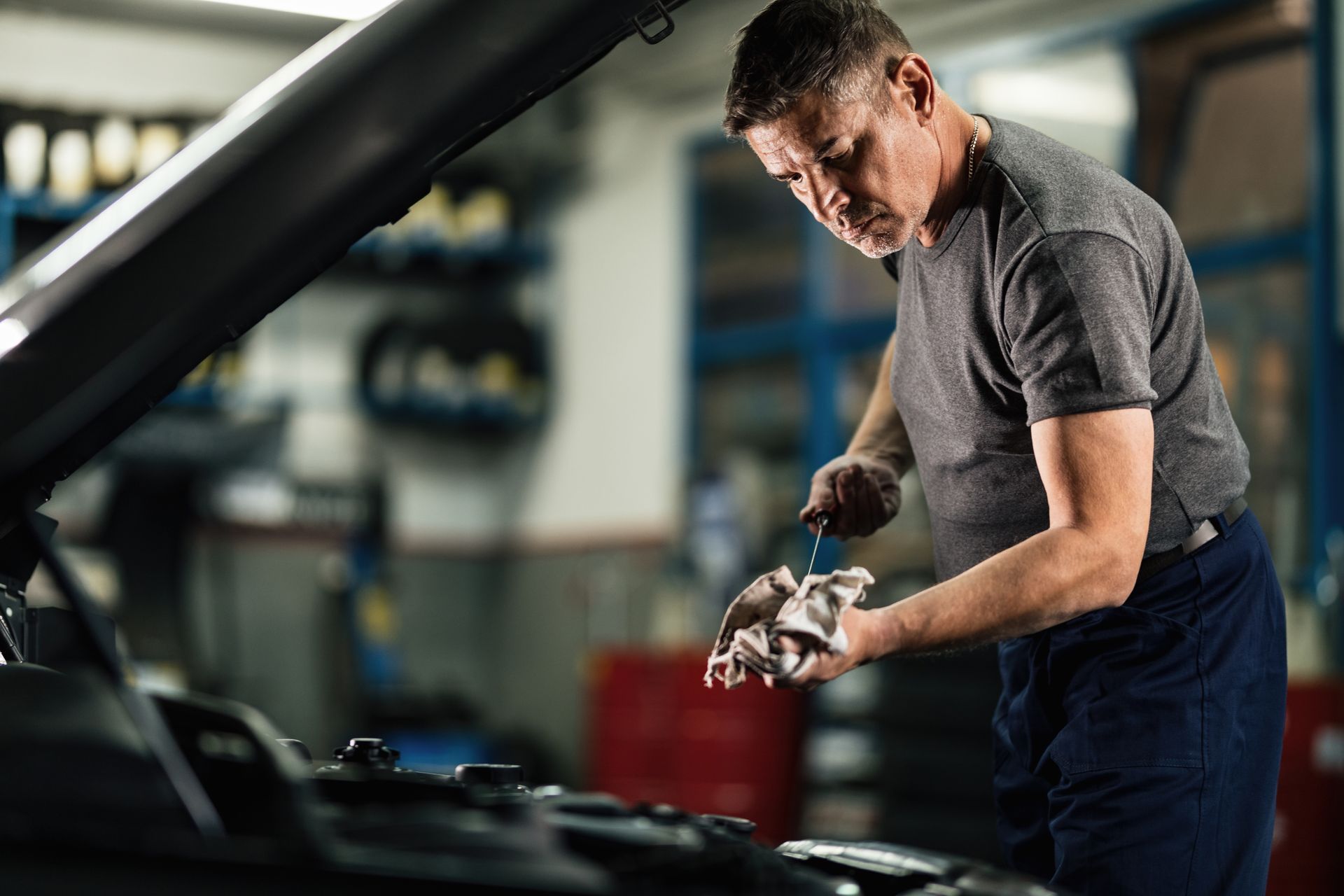 Mid adult mechanic checking oil level in car engine at auto repair shop. Mid adult mechanic checking oil level in car engine at auto repair shop.