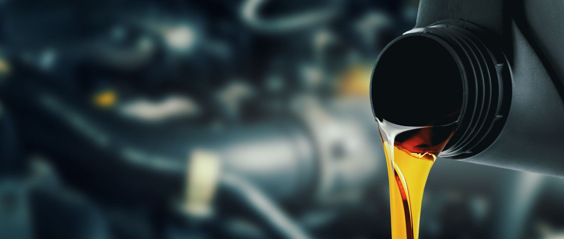 Motor oil being poured from a container with a blurred engine in the background.