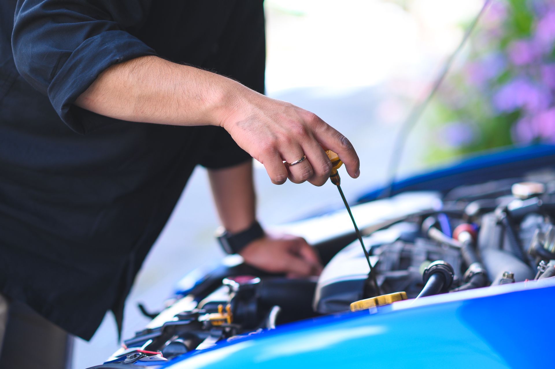 A man is checking the oil in his car with a screwdriver.