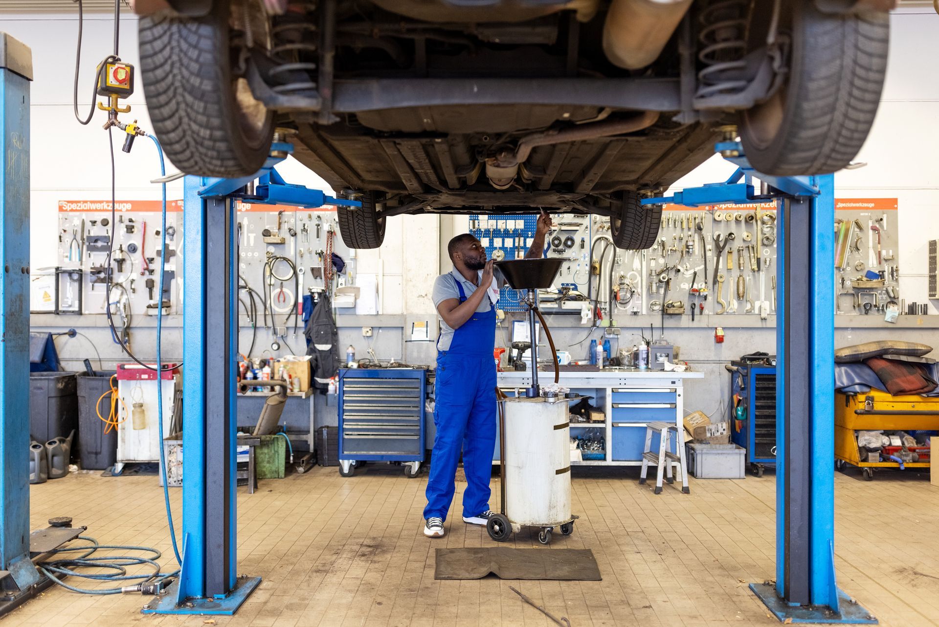 Car mechanic replacing oil from motor engine at garage.