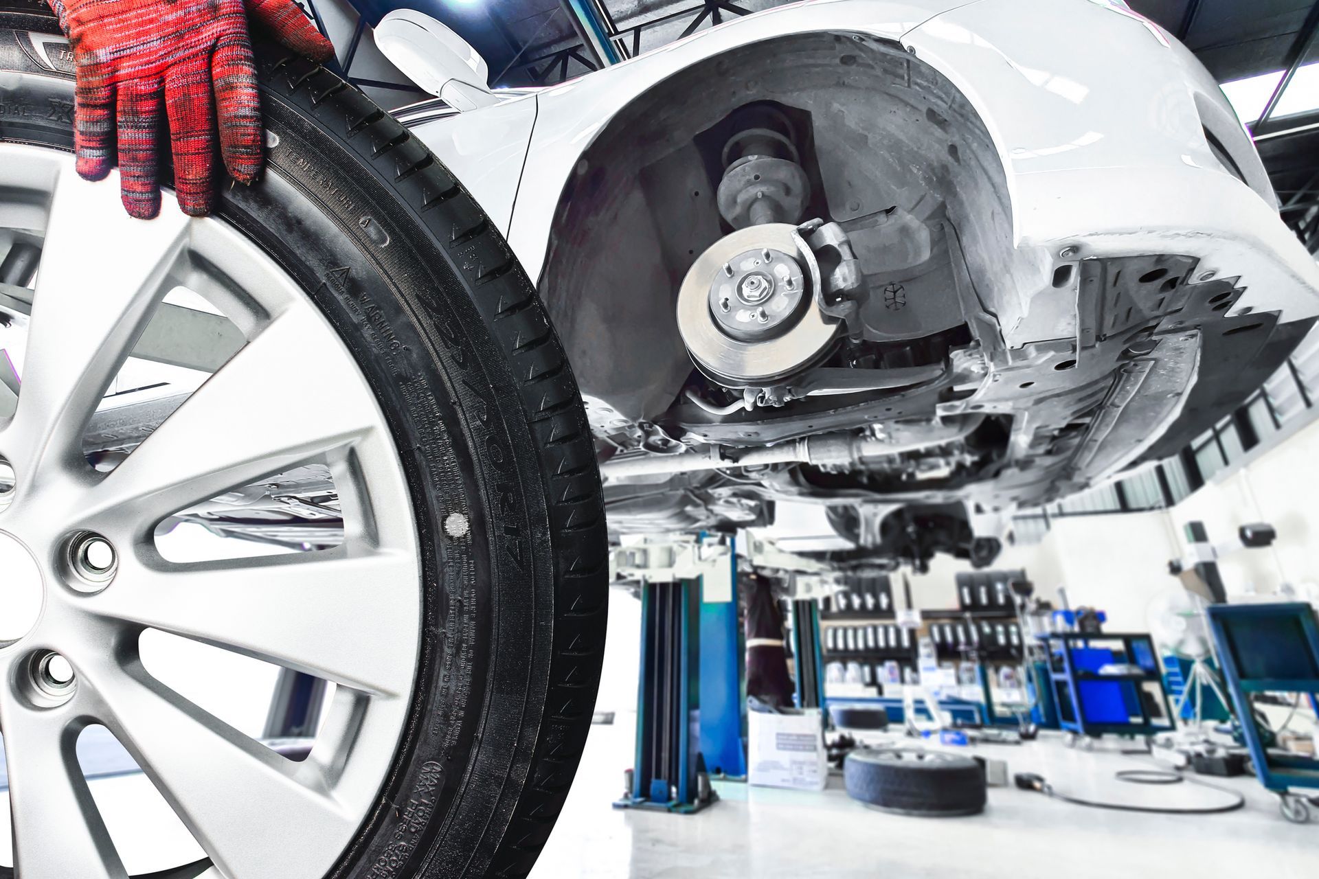 A mechanic's hand holds a car wheel removed from a white car elevated on a lift.