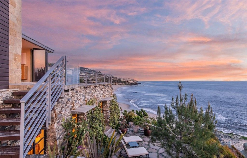 A house on a cliff overlooking the ocean at sunset.