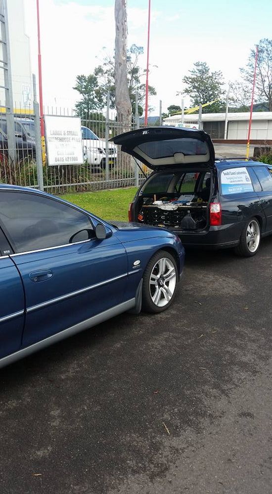 A blue car is parked next to a Black Car With the Trunk Open — South Coast Locksmiths in Fairy Meadow, NSW