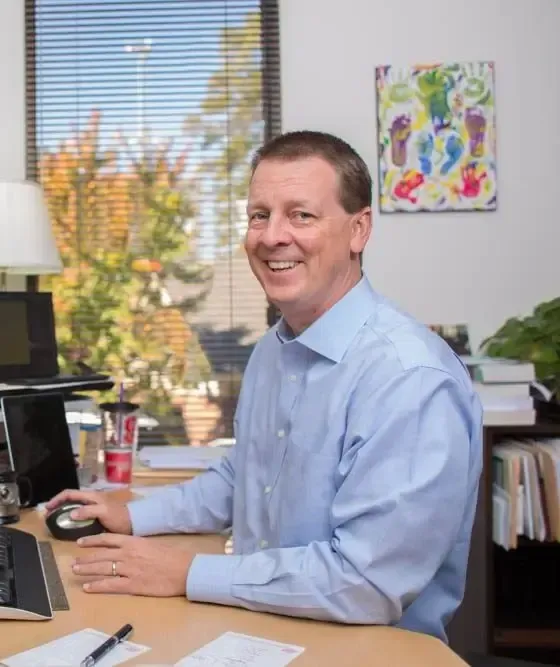 Row houses with various colors and dormer windows line a street with parked cars on both sides.