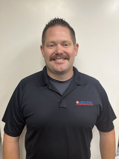 Man with a mustache wearing a black polo shirt, smiling, in front of a white wall.