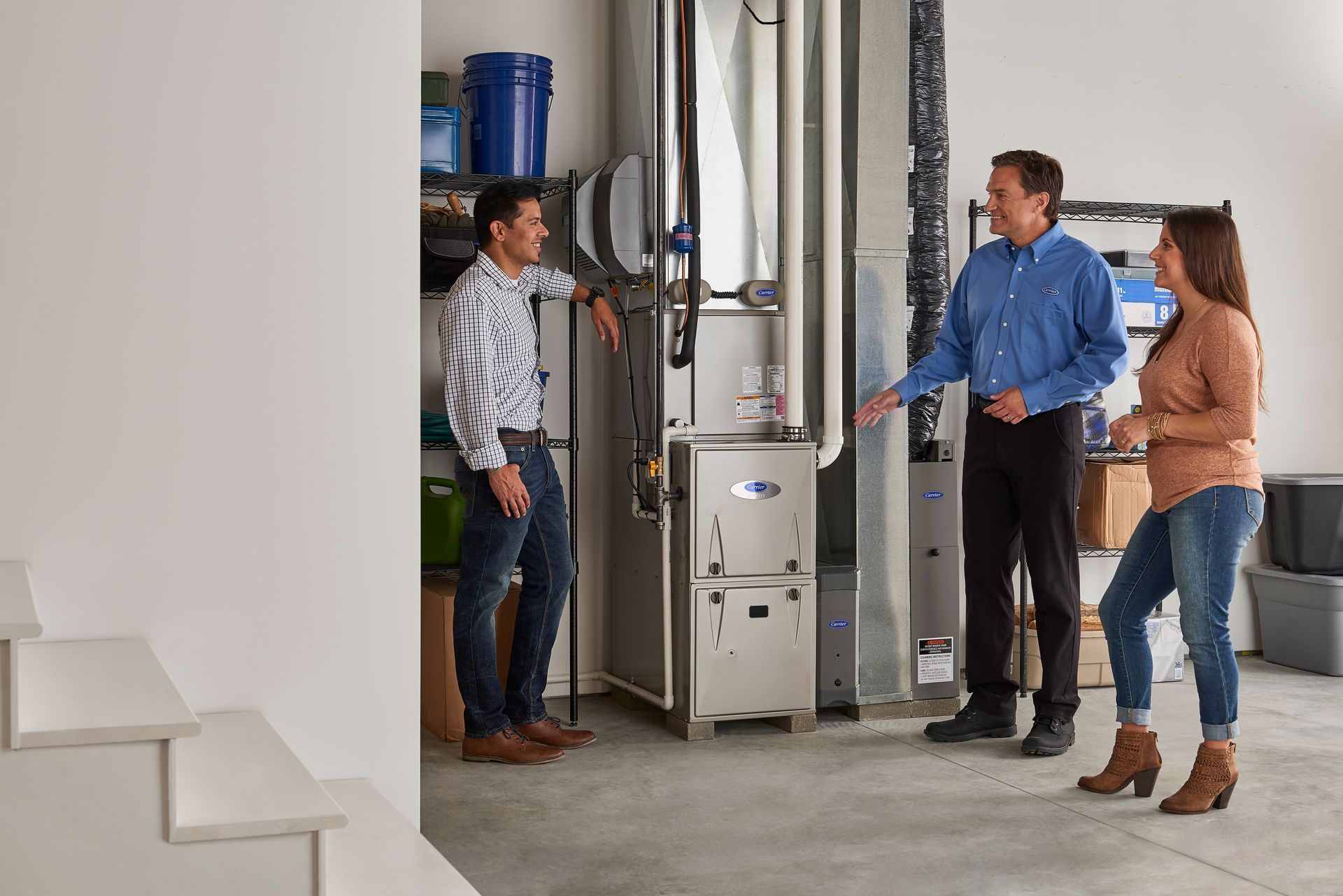 Three people discussing a furnace in a utility room. The person in blue points to the equipment.