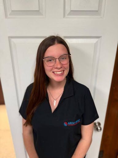 Woman with glasses and a black shirt smiling in front of a white door.