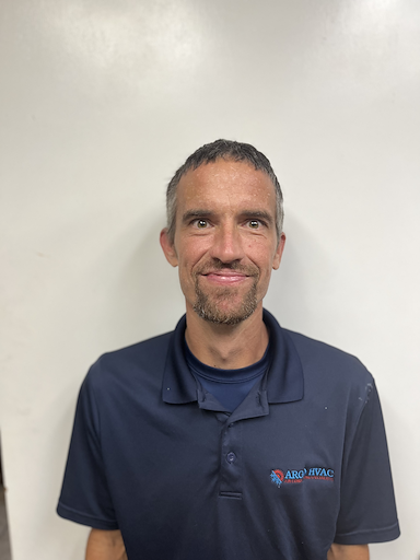 Man in blue polo shirt smiling in front of a white wall.