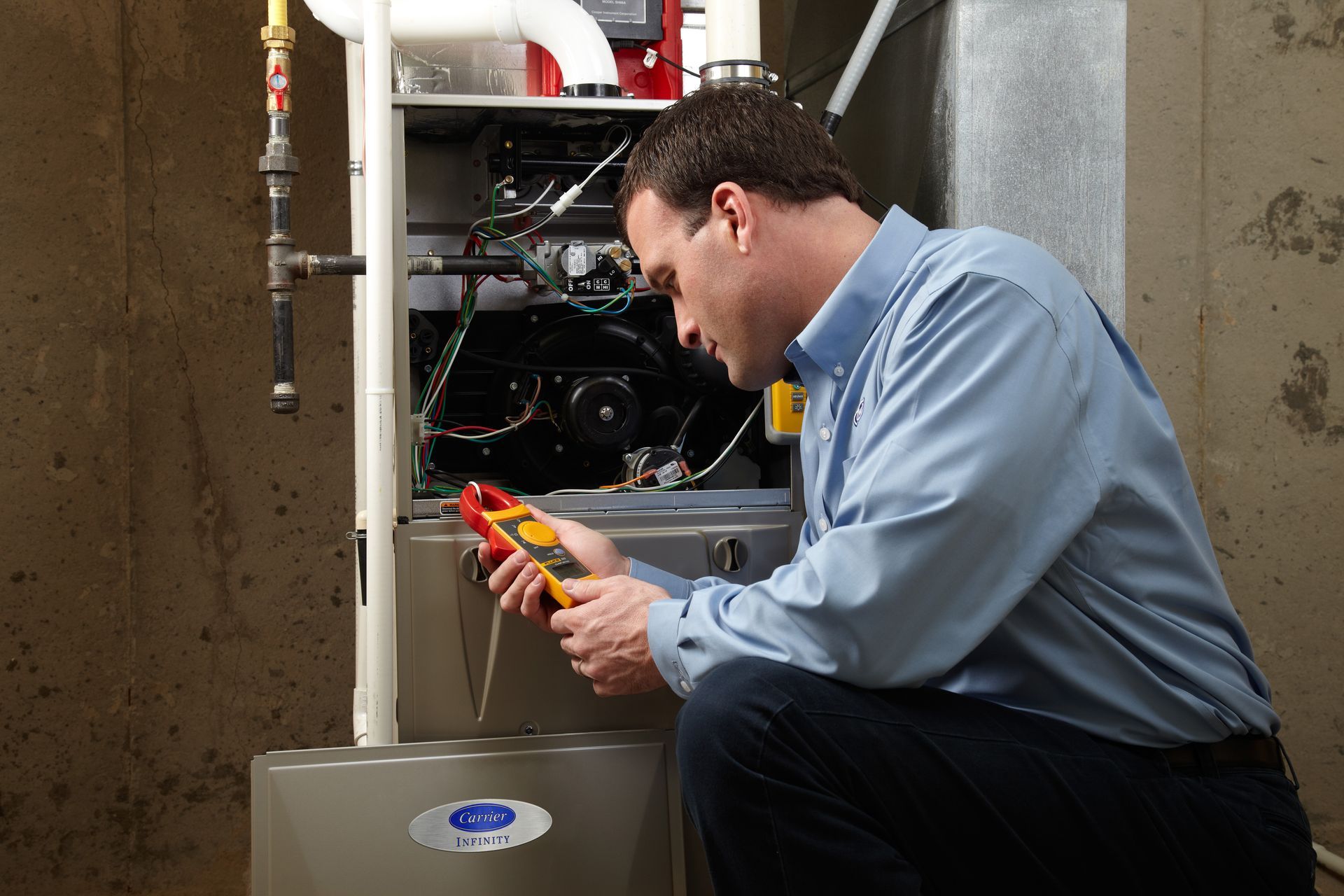 HVAC technician inspecting furnace with a flashlight. He's wearing a blue shirt and is in a utility room.