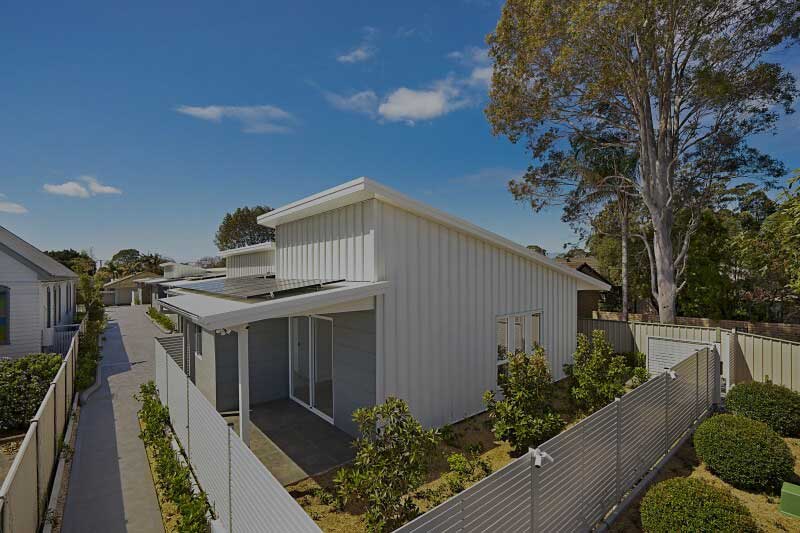 Concrete pathway through residential community of duplex houses with white fence on the side
