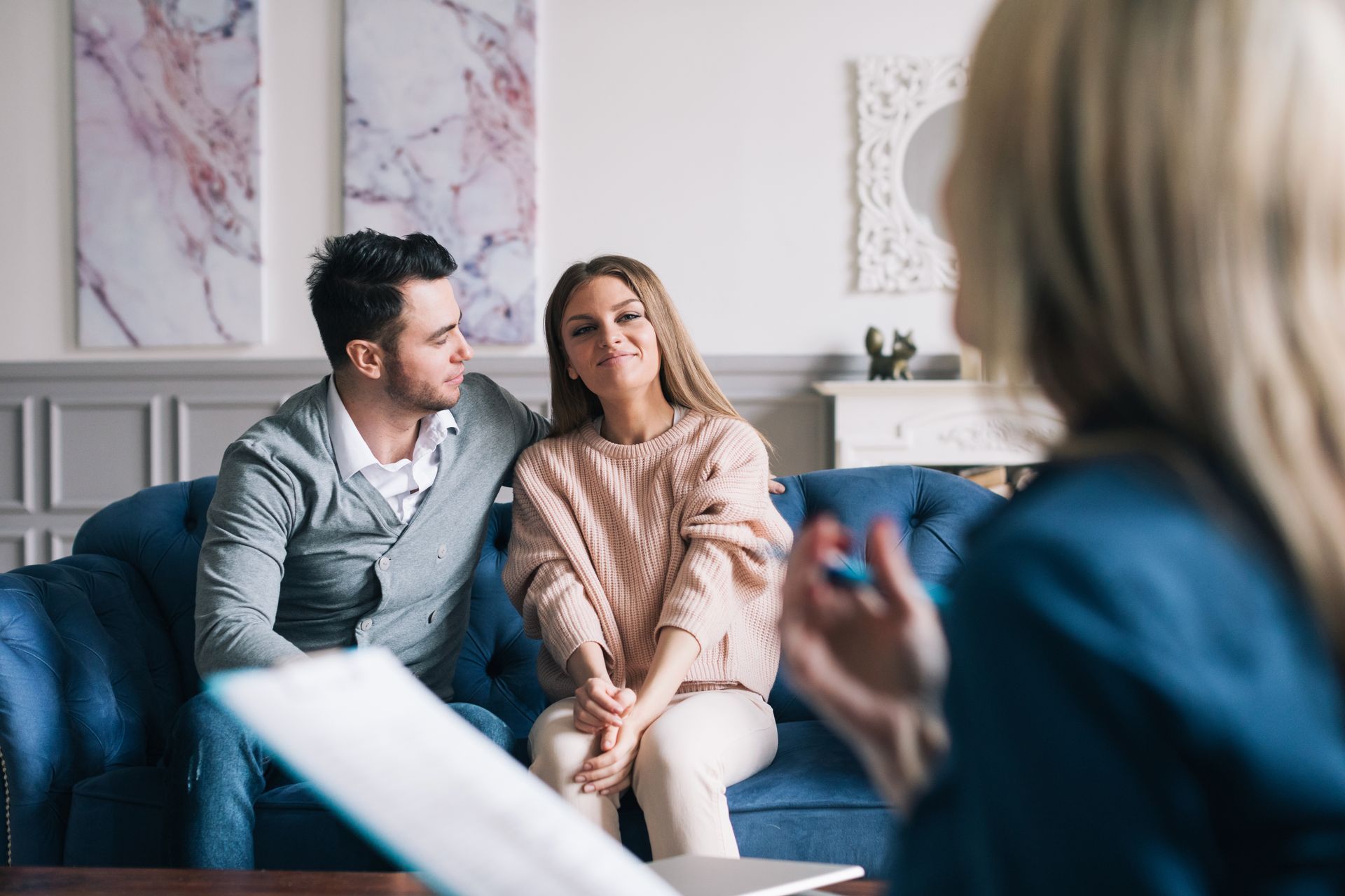 Couple seated on a couch in a counseling session, listening to a therapist in the foreground. Couple seated on a couch in a counseling session, listening to a therapist in the foreground.