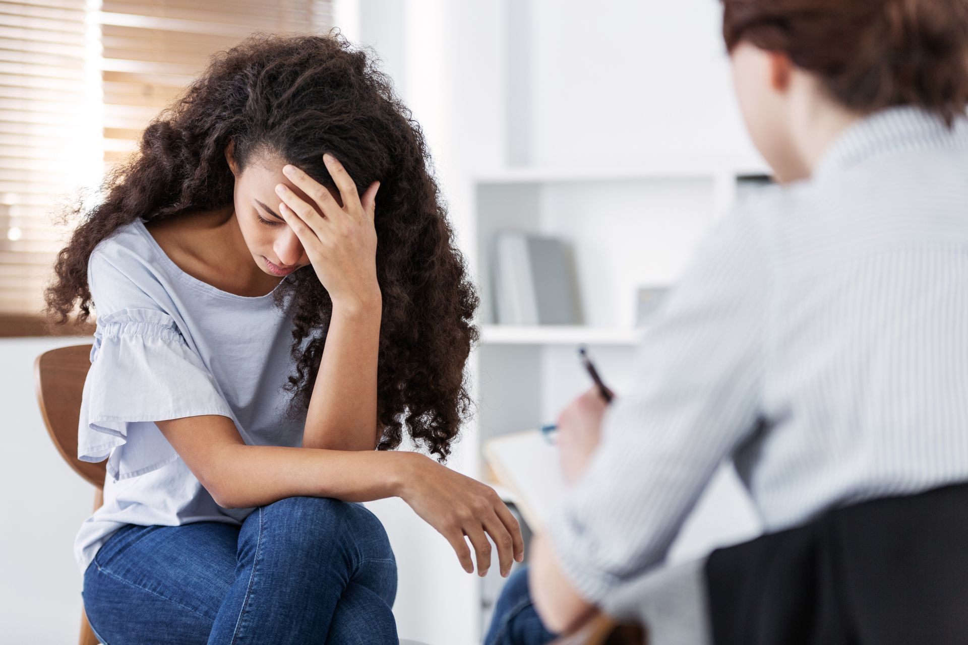 Person sitting with head in hands during a counseling session while another person listens nearby