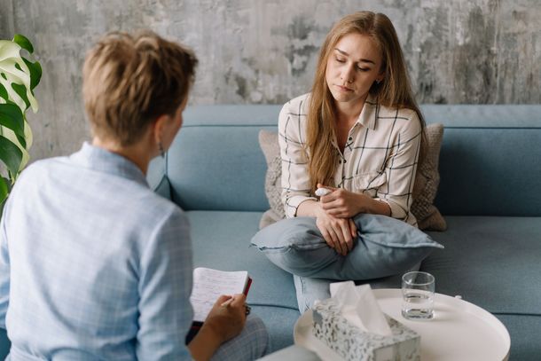 Therapist talking with a client in a bright counseling room, seated on blue and white furniture. Therapist talking with a client in a bright counseling room, seated on blue and white furniture.