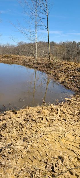 Muddy pond in the middle of a dirt field with trees in the background - Campbellsburg, IN | Twisted Electric LLC 