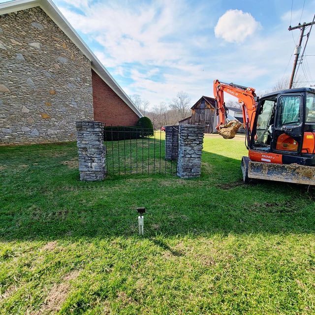 Small excavator digging a hole in the grass with steel and brick fence - Campbellsburg, IN | Twisted Electric LLC 