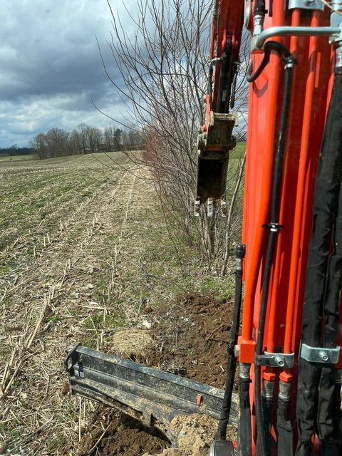Red excavator is digging a hole in a empty field - Campbellsburg, IN | Twisted Electric LLC 