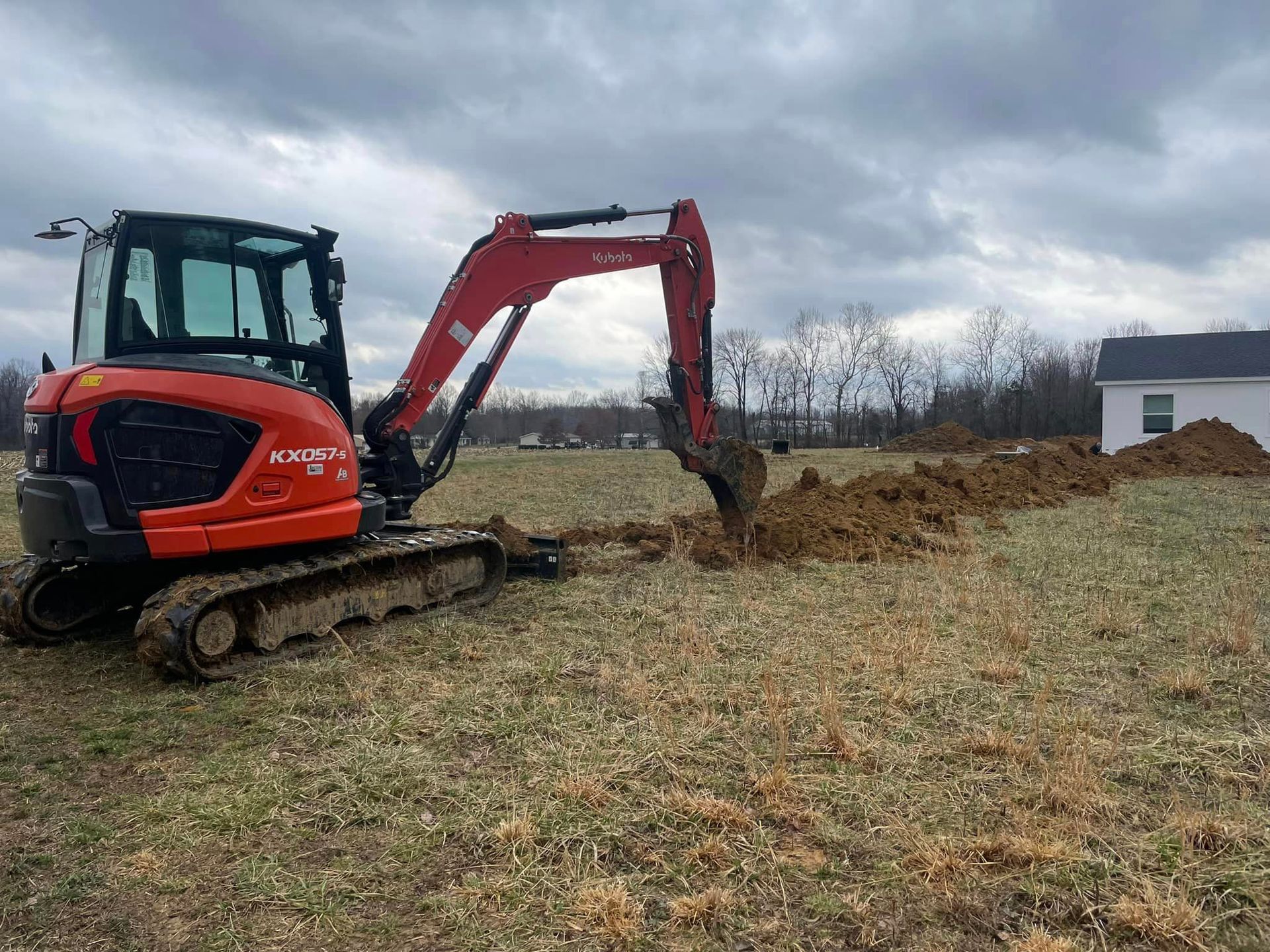 A small red excavator is digging a hole in a field.