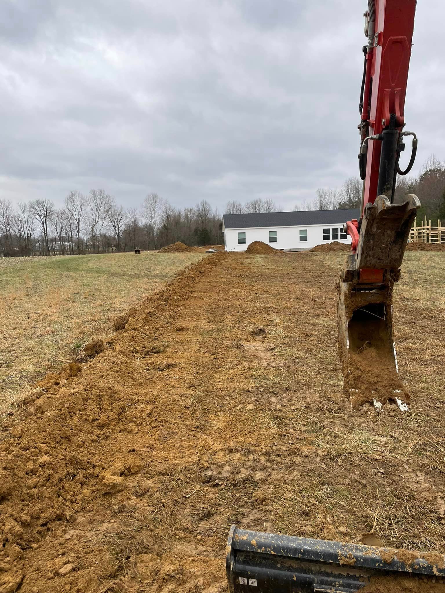 A red excavator is digging a hole in the dirt in a field.