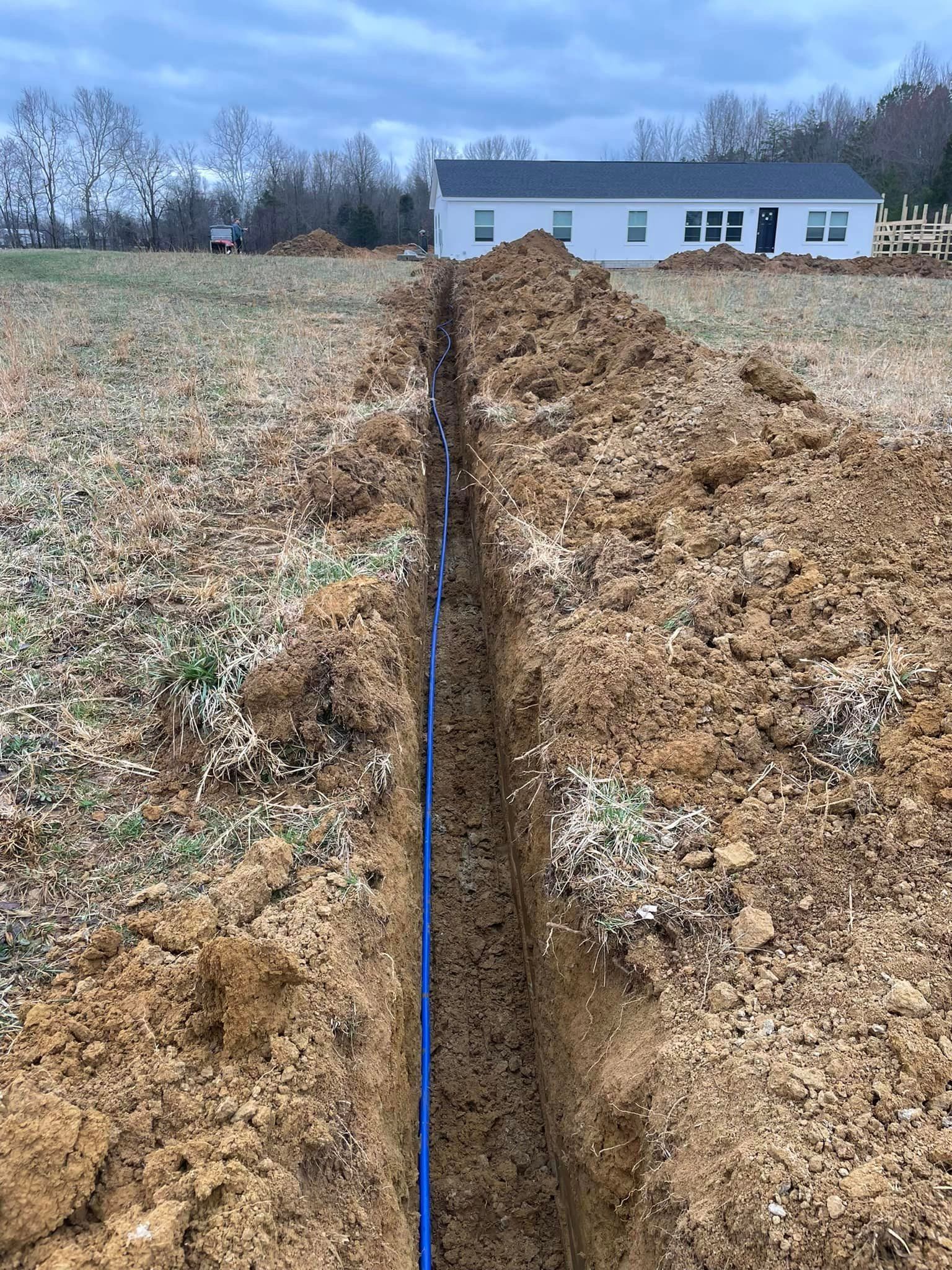 A large trench in the middle of a field with a house in the background.