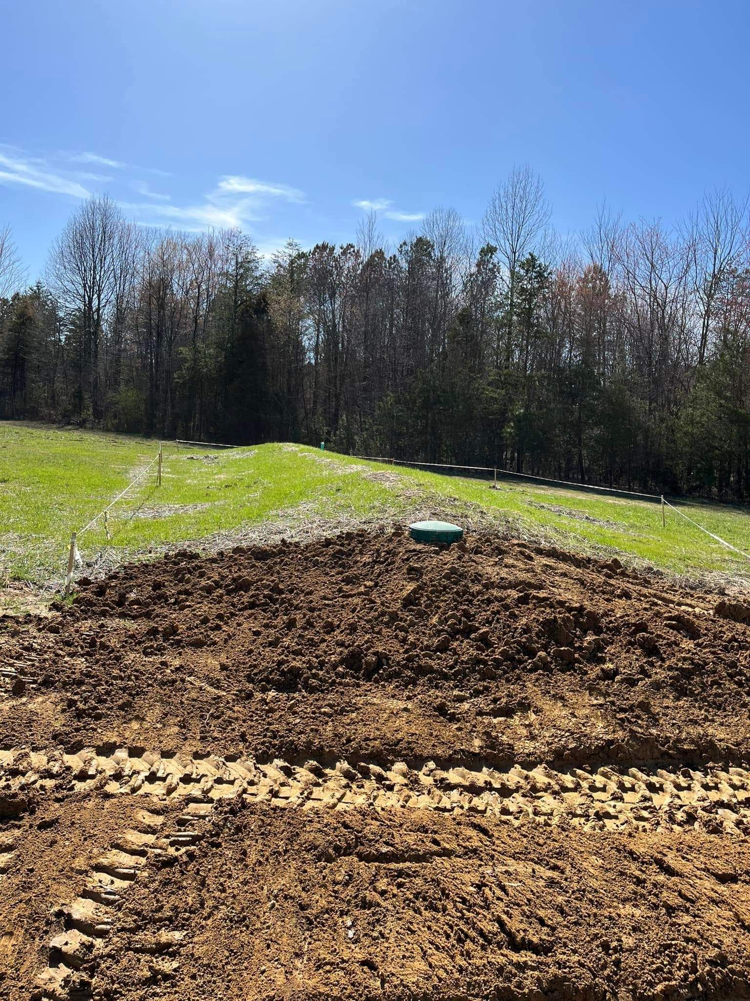 A large pile of dirt in a field with trees in the background.