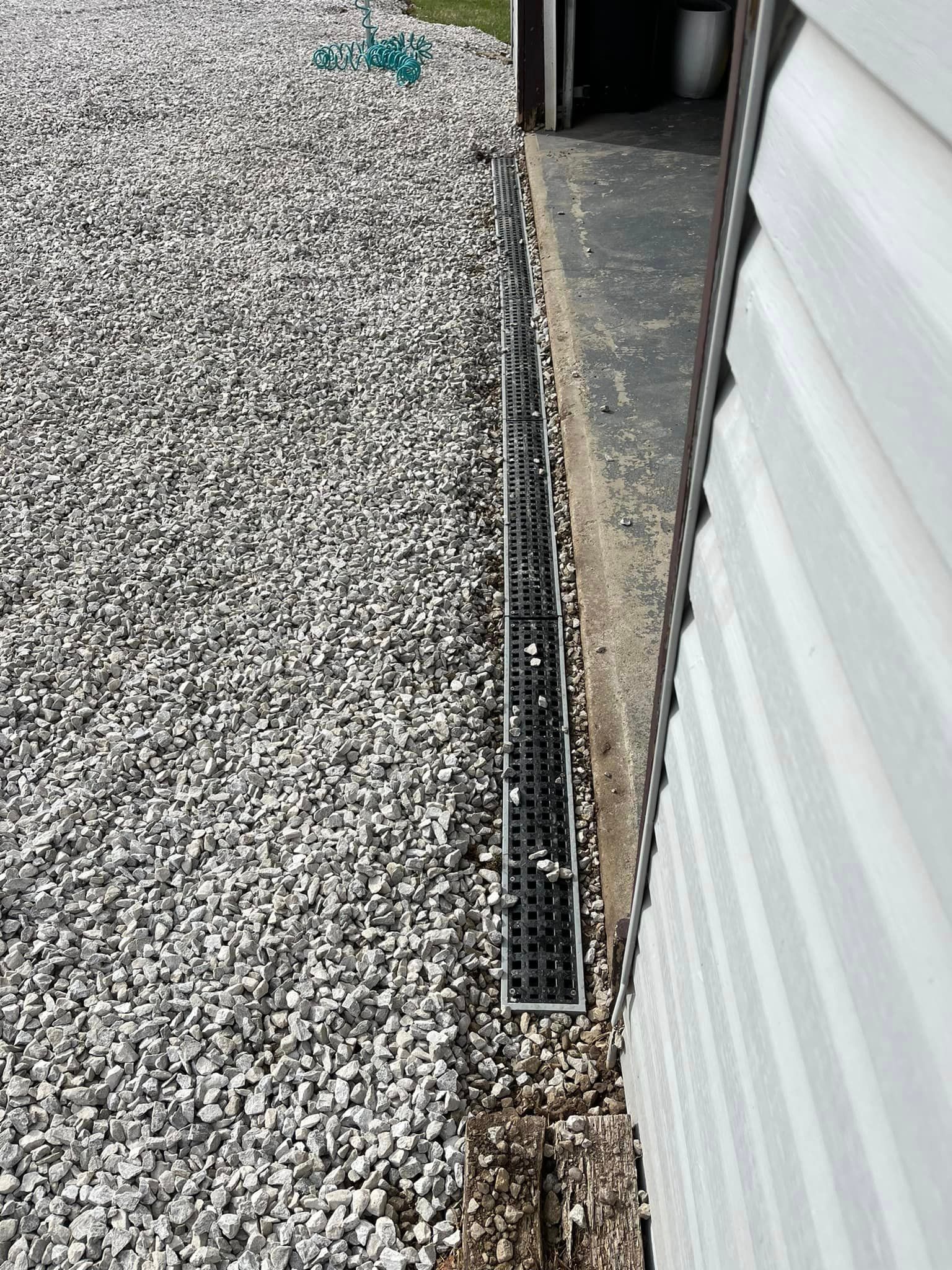 A drain on the side of a house next to a gravel driveway.