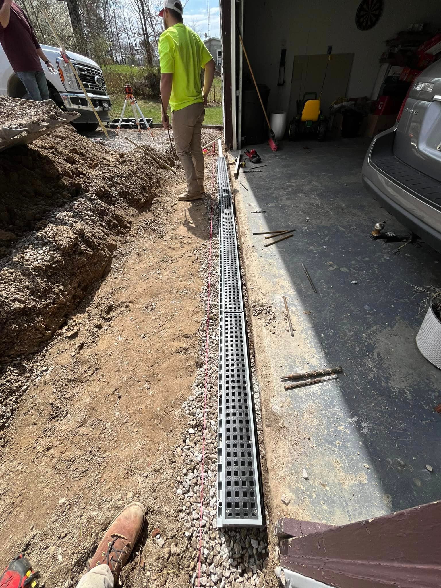 A man is standing next to a drain in a driveway next to a garage.