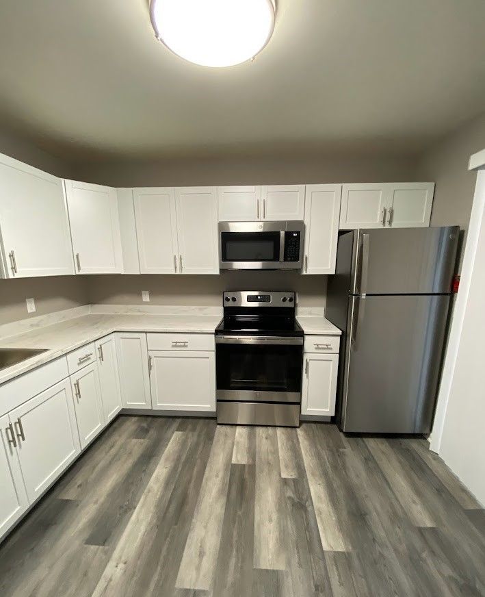 A kitchen with white cabinets , stainless steel appliances , a refrigerator , stove , microwave and sink.