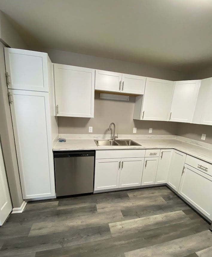 A kitchen with white cabinets , a sink , and a dishwasher.