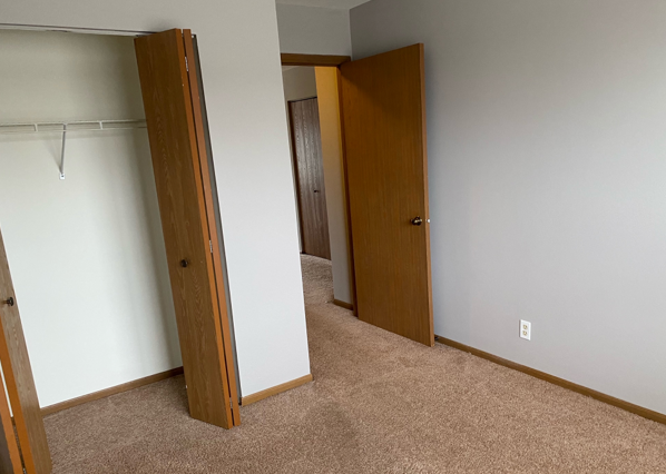 An empty bedroom with a closet and two doors.