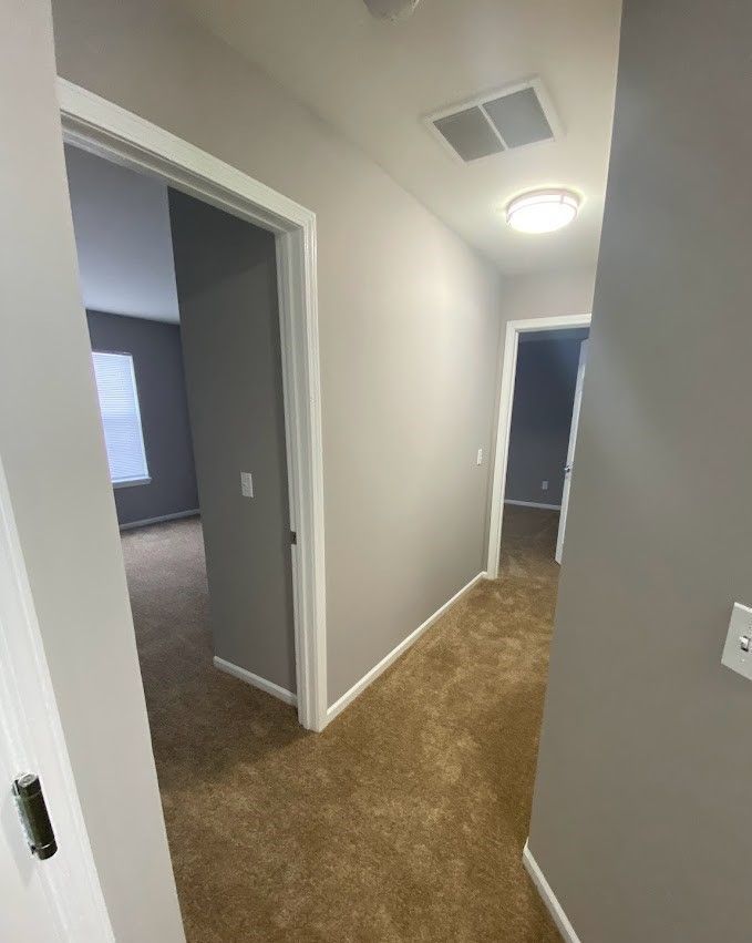 A hallway in a house with a carpeted floor and a light on the ceiling.