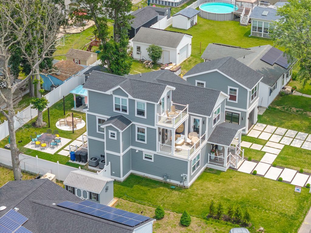 Aerial view of a gray multi-story house with balconies and a yard, in a residential neighborhood.