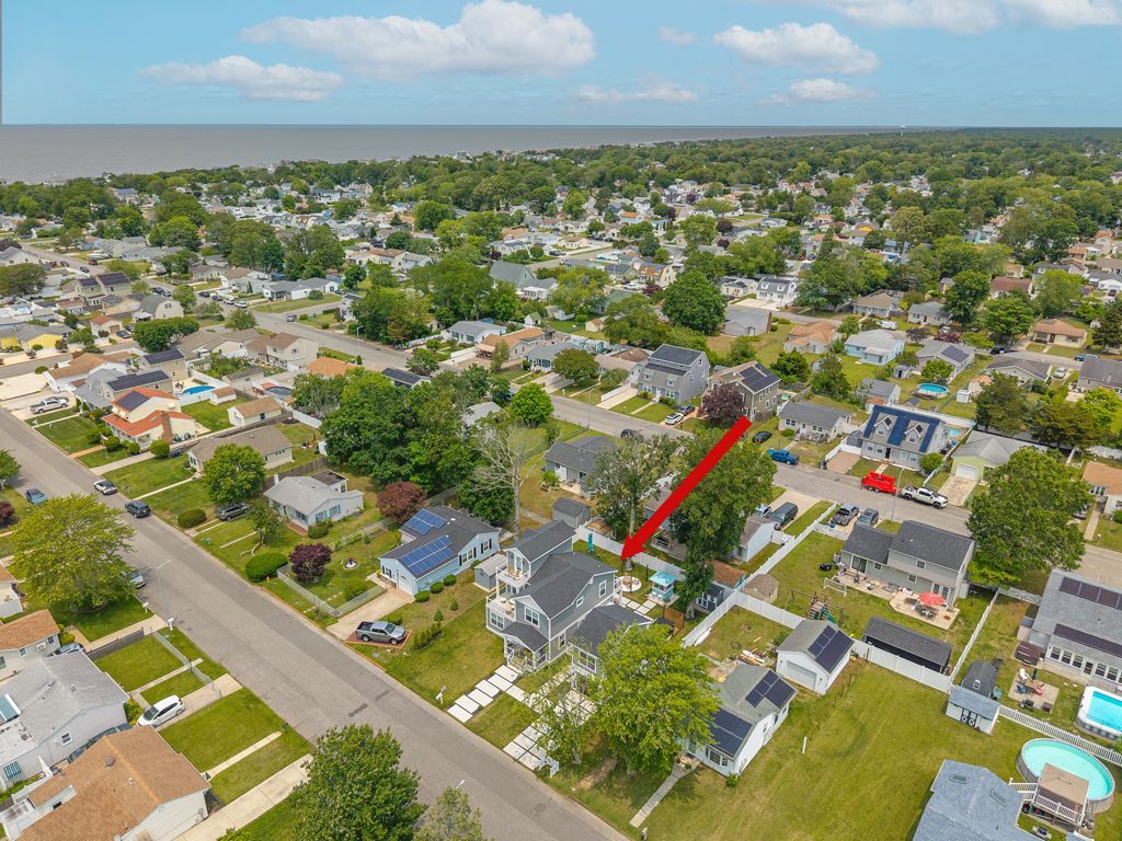 Aerial view of a residential neighborhood with houses, trees, and a body of water in the distance.