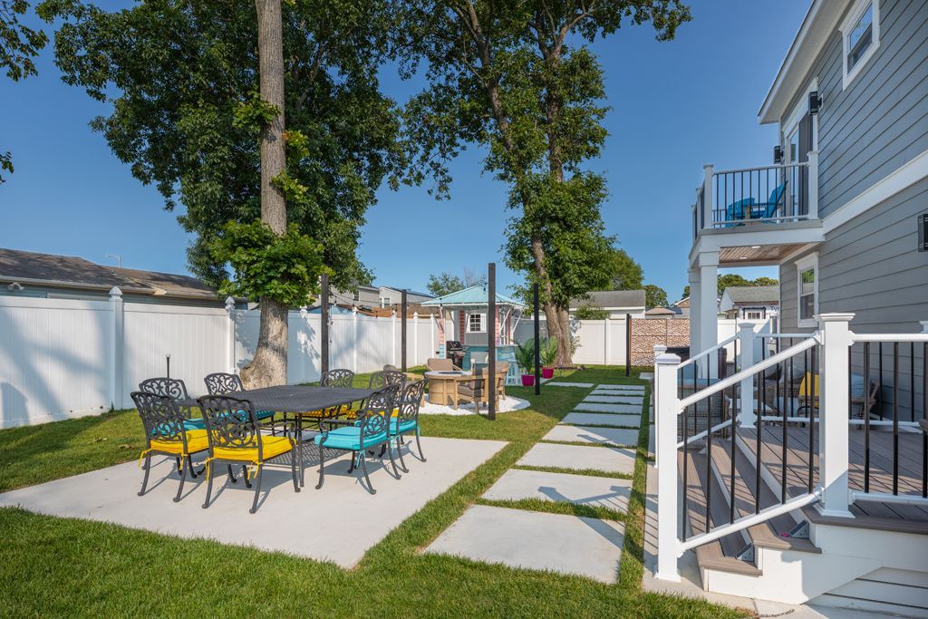 Outdoor patio with dining table and colorful chairs, next to a house with steps.